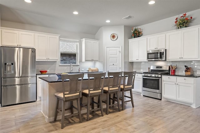 kitchen with a kitchen bar, dark countertops, a kitchen island, white cabinetry, and stainless steel appliances