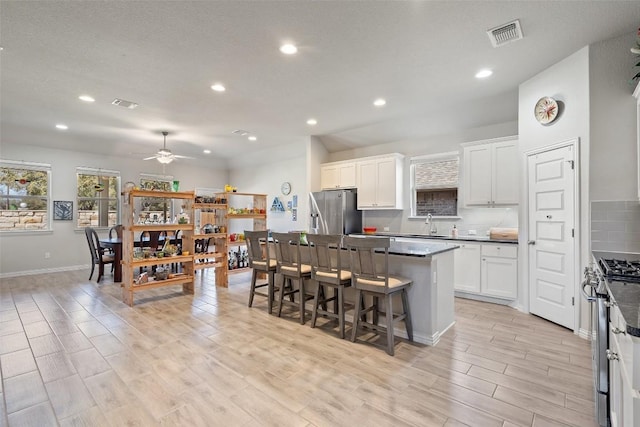 kitchen featuring light wood finished floors, a kitchen island, stainless steel appliances, white cabinets, and backsplash