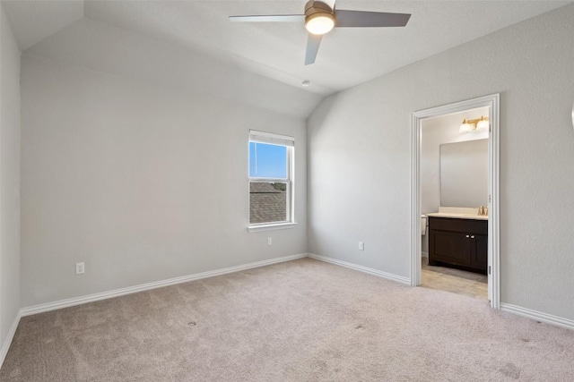 unfurnished bedroom featuring baseboards, ceiling fan, vaulted ceiling, ensuite bathroom, and light colored carpet