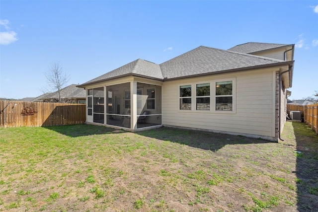 rear view of house with a sunroom, roof with shingles, cooling unit, a fenced backyard, and a yard