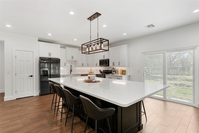 kitchen with visible vents, black appliances, a center island, a breakfast bar area, and light countertops