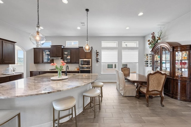 kitchen featuring a healthy amount of sunlight, a breakfast bar, dark brown cabinetry, appliances with stainless steel finishes, and backsplash