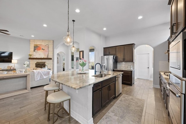 kitchen featuring a sink, backsplash, stainless steel appliances, arched walkways, and dark brown cabinets