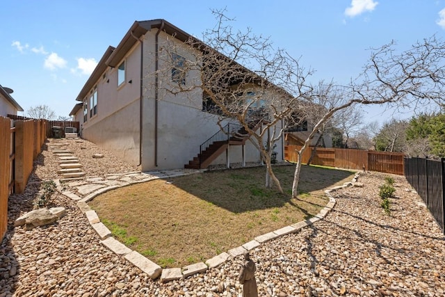 view of side of property featuring stairway, a lawn, and a fenced backyard