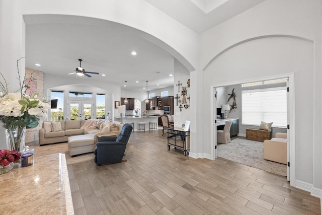 living room with a ceiling fan, baseboards, recessed lighting, arched walkways, and light wood-type flooring