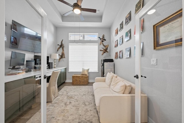 office space with wood finished floors, a tray ceiling, baseboards, and ceiling fan