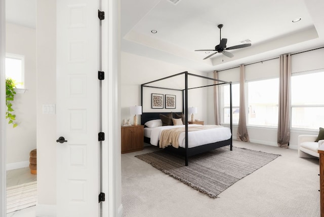 bedroom with a tray ceiling, baseboards, and light colored carpet