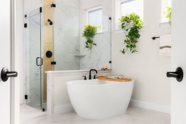 bathroom featuring marble finish floor, a freestanding bath, a shower stall, and baseboards