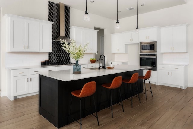 kitchen featuring wood finished floors, visible vents, a sink, appliances with stainless steel finishes, and wall chimney range hood