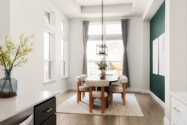 dining room featuring a tray ceiling, baseboards, and light wood-style flooring