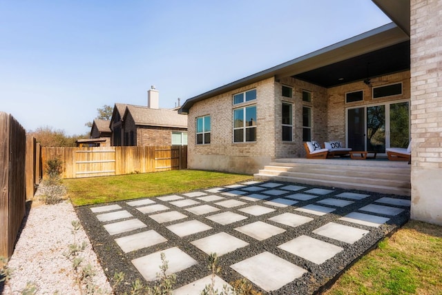 rear view of house featuring a ceiling fan, a patio, a fenced backyard, a yard, and brick siding