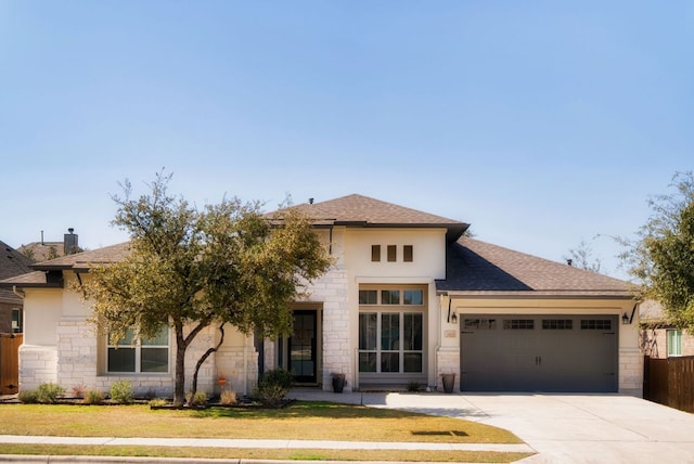 prairie-style house with a shingled roof, a front lawn, concrete driveway, a garage, and stone siding