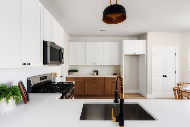 kitchen featuring appliances with stainless steel finishes, white cabinetry, light countertops, and a sink