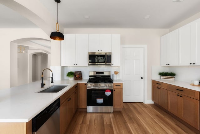 kitchen featuring light countertops, light wood-style flooring, appliances with stainless steel finishes, arched walkways, and a sink