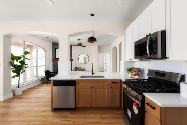 kitchen featuring a sink, light wood-style floors, appliances with stainless steel finishes, a peninsula, and light countertops