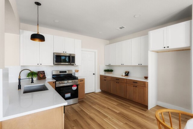 kitchen with visible vents, light countertops, light wood-style flooring, stainless steel appliances, and a sink