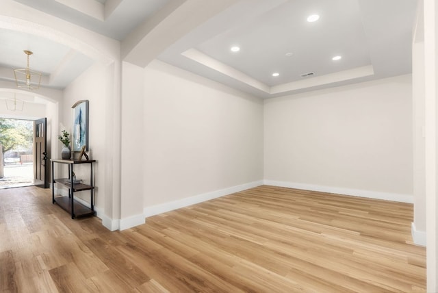 spare room featuring arched walkways, visible vents, a raised ceiling, and light wood-style floors