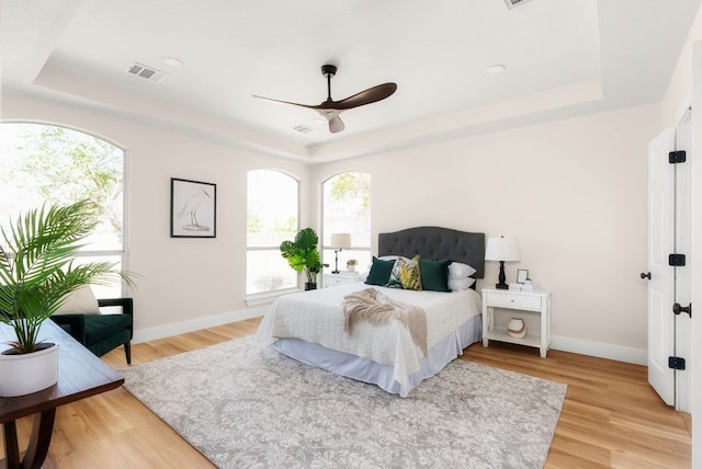 bedroom with a raised ceiling, light wood-style floors, baseboards, and visible vents