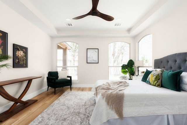 bedroom featuring a tray ceiling, wood finished floors, baseboards, and visible vents