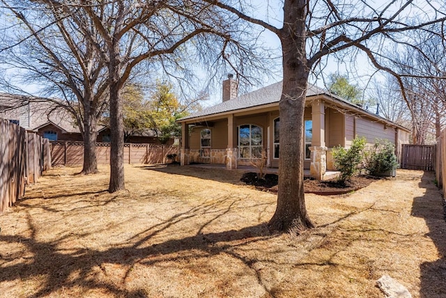 view of side of home featuring a porch, a fenced backyard, and a chimney