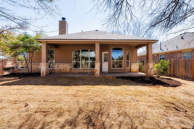 back of property with fence, stone siding, roof with shingles, and a chimney