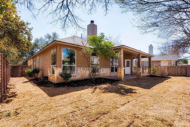 rear view of house with stone siding, a chimney, and a fenced backyard