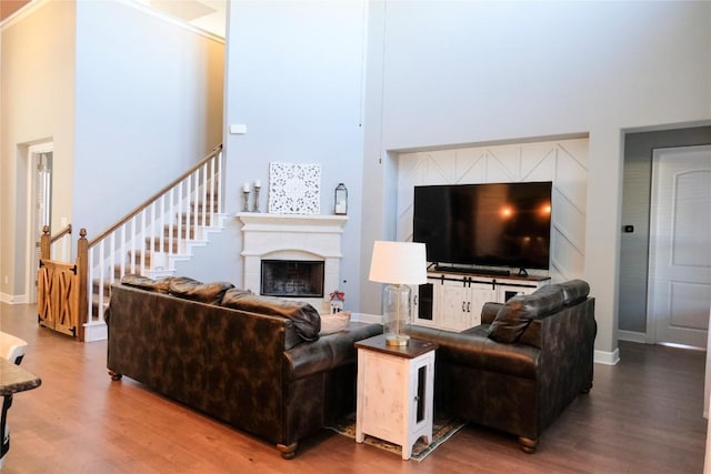 living area featuring a fireplace, a high ceiling, baseboards, and wood finished floors