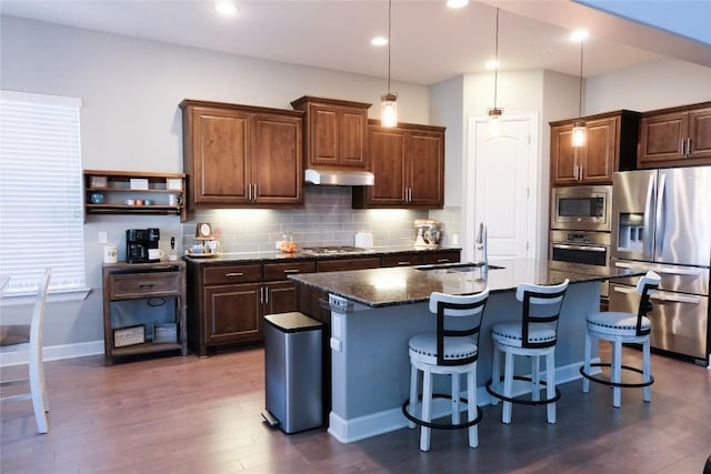 kitchen featuring a sink, backsplash, under cabinet range hood, stainless steel appliances, and dark wood-style flooring