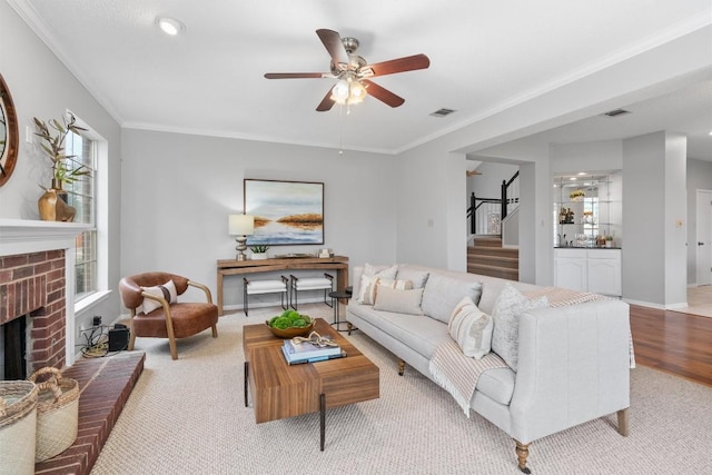 living area featuring a brick fireplace, stairs, crown molding, and ceiling fan