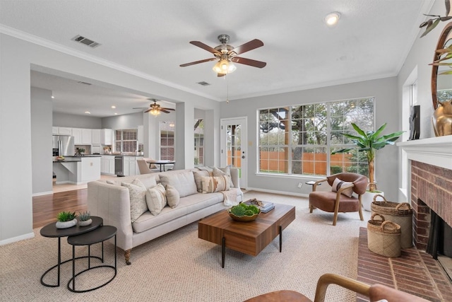 living area with visible vents, a ceiling fan, a brick fireplace, and crown molding