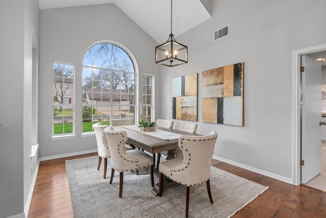 dining room featuring visible vents, baseboards, hardwood / wood-style flooring, a notable chandelier, and high vaulted ceiling