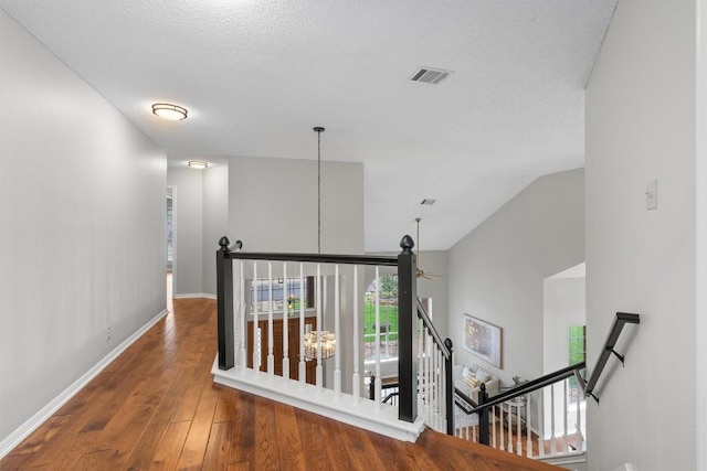 hallway with visible vents, an upstairs landing, wood-type flooring, an inviting chandelier, and baseboards