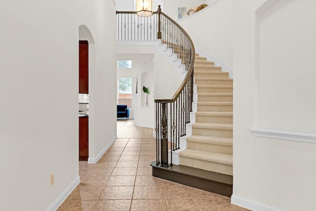 entryway with arched walkways, baseboards, stairs, and a towering ceiling