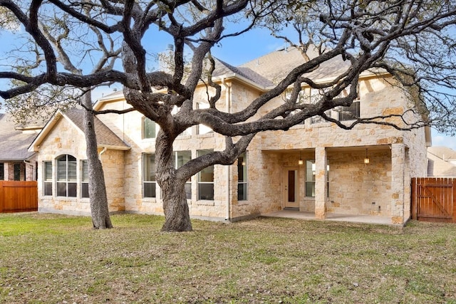 rear view of house with a patio area, stone siding, a yard, and fence