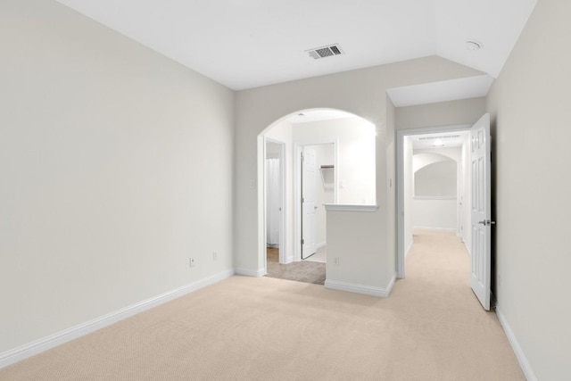 empty room with visible vents, baseboards, vaulted ceiling, light carpet, and arched walkways