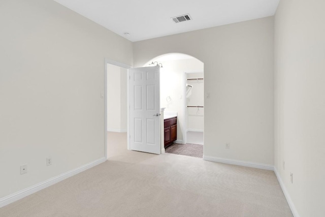 empty room with arched walkways, visible vents, light colored carpet, and baseboards