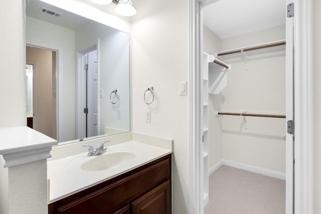 bathroom with vanity, a spacious closet, baseboards, and visible vents