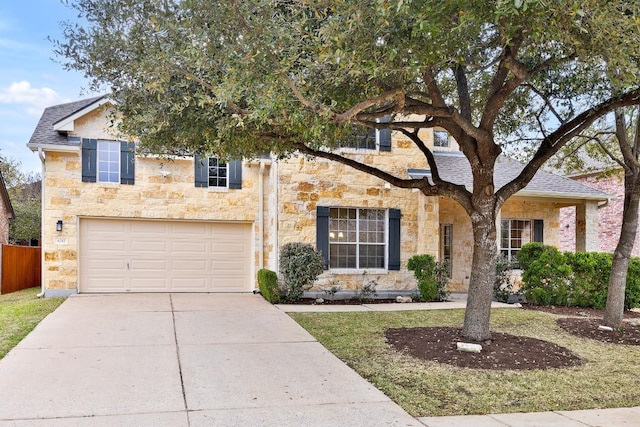 traditional-style home featuring fence, driveway, a shingled roof, a garage, and stone siding