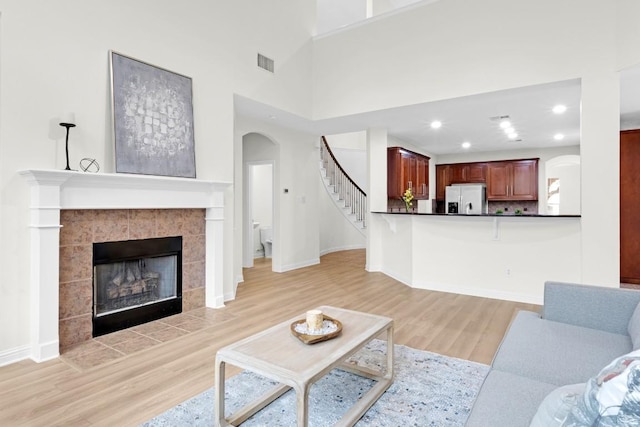 living room featuring visible vents, a tiled fireplace, recessed lighting, light wood-style floors, and stairs