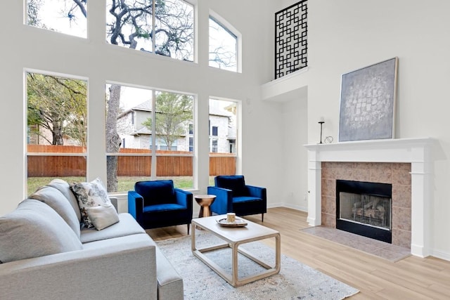 living area featuring baseboards, a high ceiling, wood finished floors, and a tiled fireplace