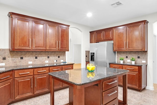 kitchen with tasteful backsplash, visible vents, stainless steel fridge with ice dispenser, dark stone counters, and arched walkways