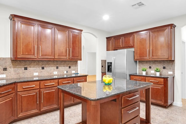6717 Blissfield Dr, Austin, TX 78739 - kitchen featuring stainless steel fridge, arched walkways, dark stone counters, backsplash, and light tile patterned floors