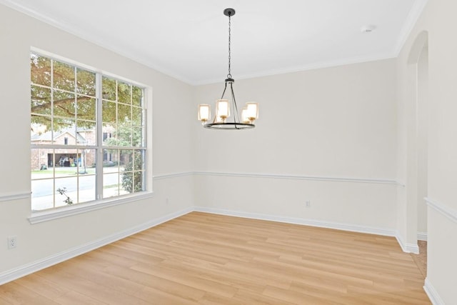 empty room with a notable chandelier, crown molding, and light wood finished floors