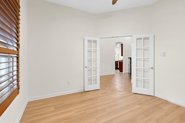 empty room featuring baseboards, arched walkways, ceiling fan, french doors, and light wood-type flooring