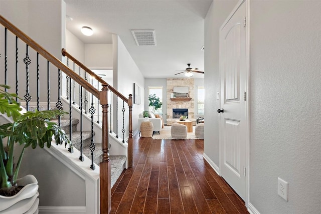 foyer entrance featuring visible vents, a ceiling fan, dark wood finished floors, a stone fireplace, and stairs