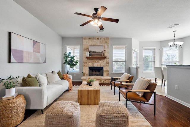 living room featuring baseboards, visible vents, a fireplace, ceiling fan with notable chandelier, and light wood-type flooring