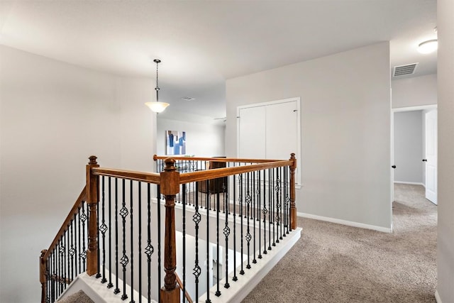 hallway with an upstairs landing, visible vents, carpet floors, and baseboards