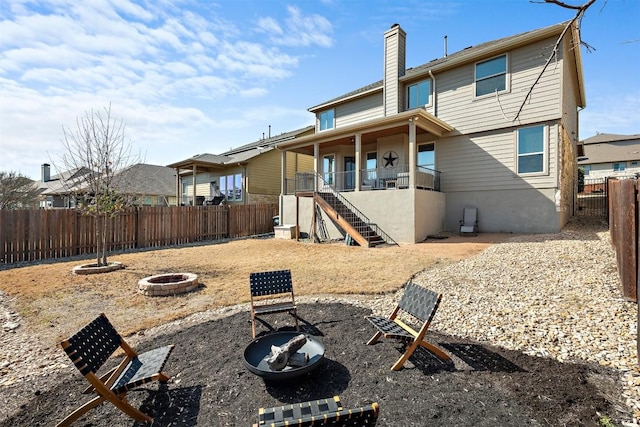 rear view of property featuring stairway, a fenced backyard, a chimney, and an outdoor fire pit