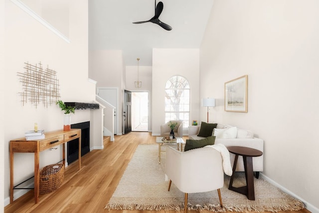 living area featuring a high ceiling, a ceiling fan, light wood-style floors, and baseboards