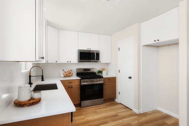 kitchen featuring light wood finished floors, a sink, stainless steel appliances, white cabinets, and light countertops